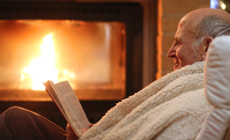 Male senior reading a book near a fireplace